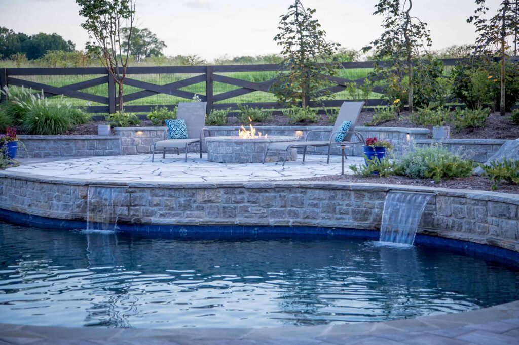 Beautiful Fire Pit on Stone Patio Above Custom Pool, Water Features | Milosi Landscaping