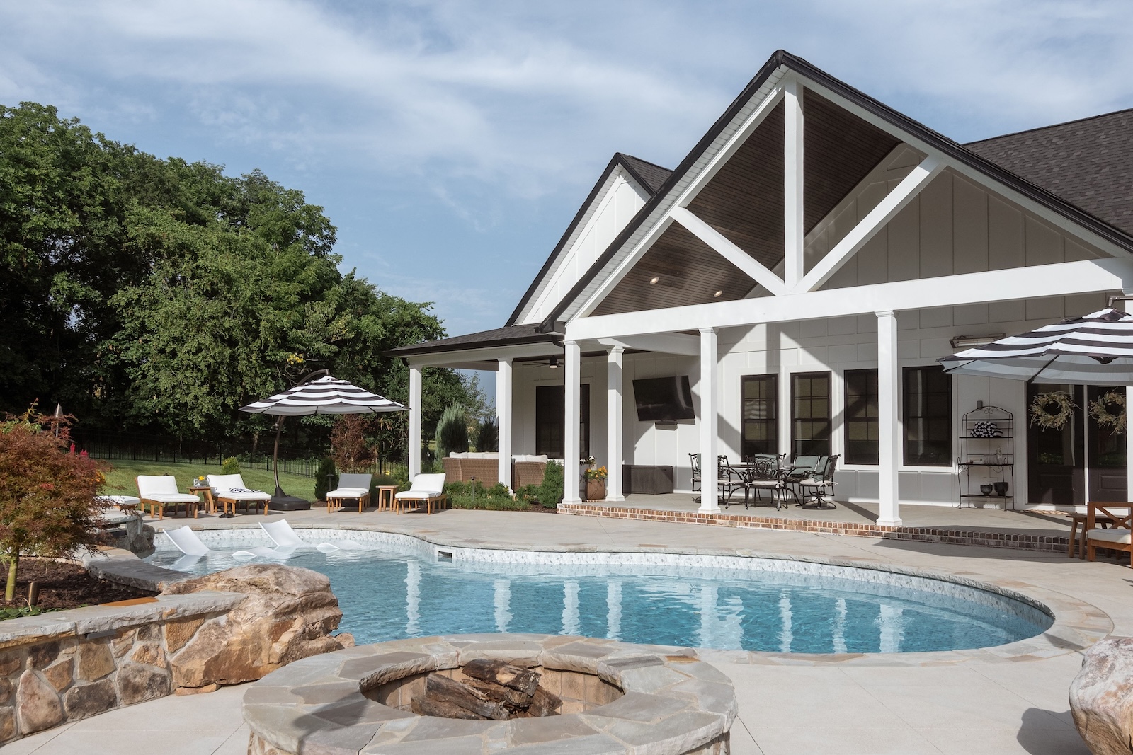 Custom Pool, Stone Fire Pit, Black & White Patio Furniture With Trees in Background | Milosi Nashville Landscaping