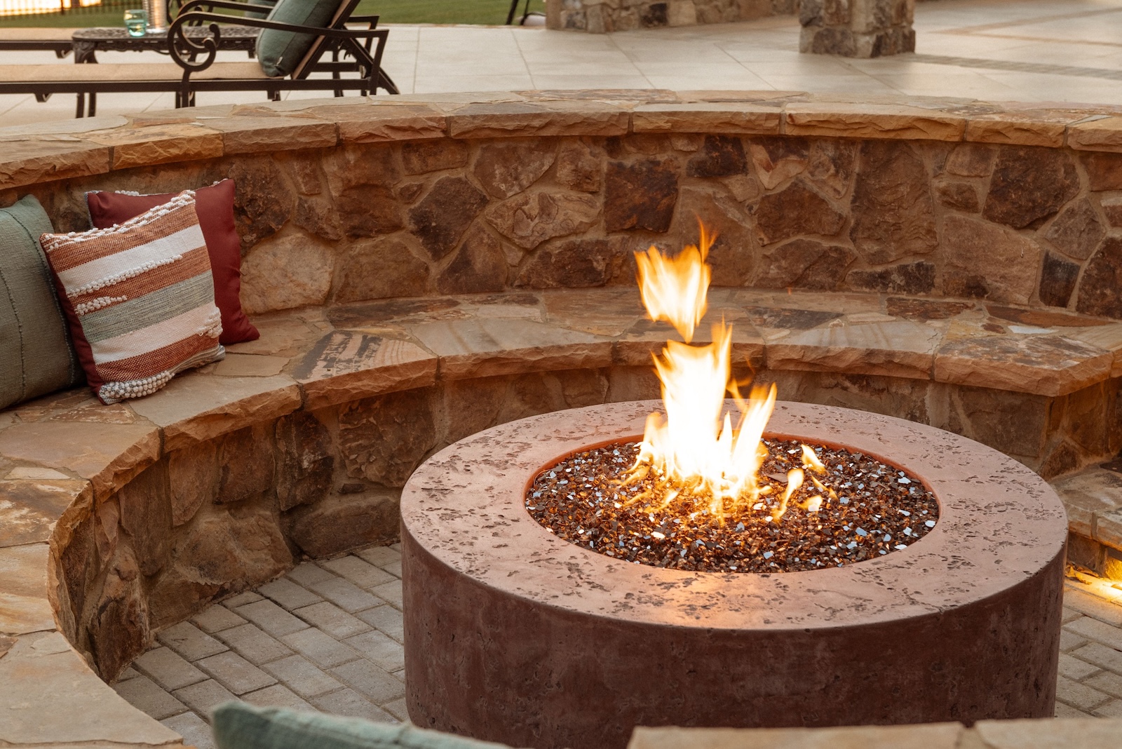 Custom stone firepit with built-in stone seating and pillows | Milosi Nashville Landscaping