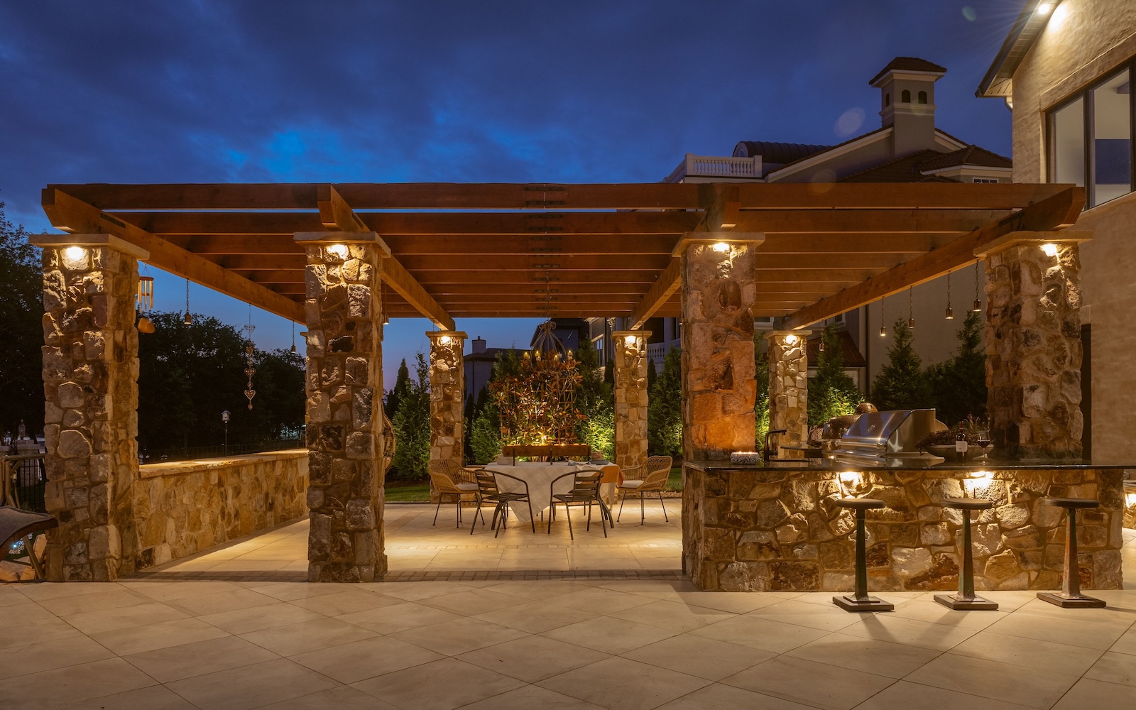 Custom Outdoor Kitchen and Dining Area Under Pergola at Night | Milosi Nashville Landscaping
