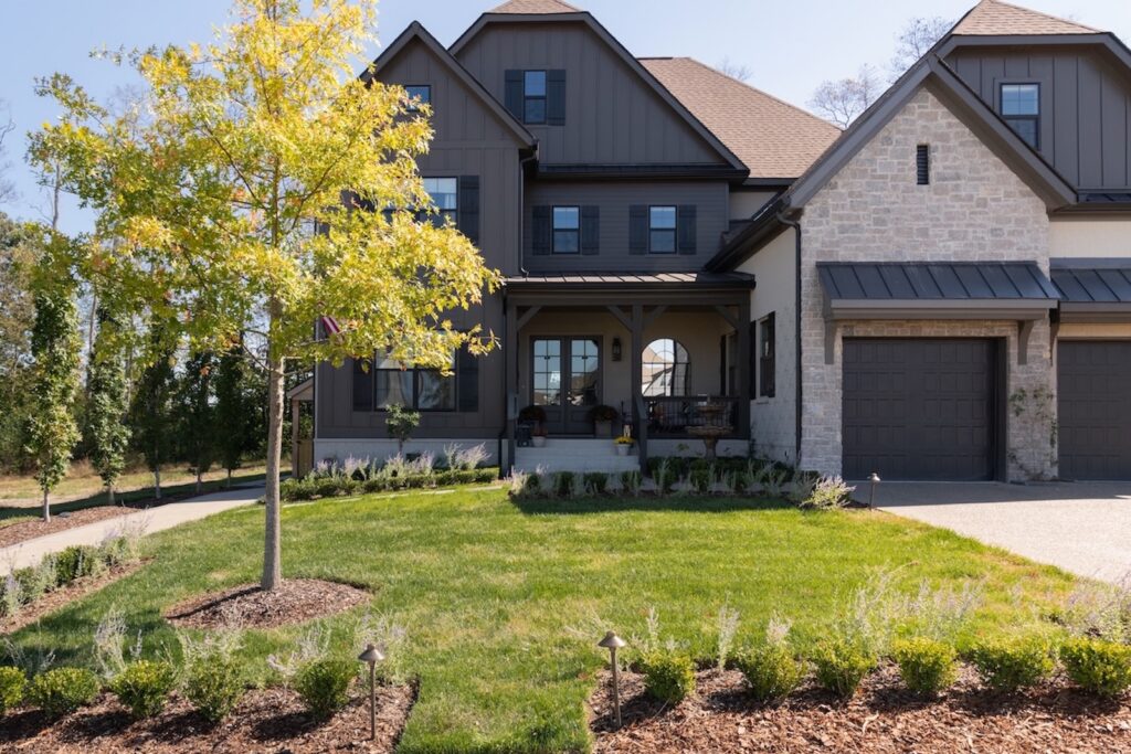 Custom Landscaped Lawn with Well Maintained Flower Beds and a Young Tree in Front of Dark & Neutral Luxury Home