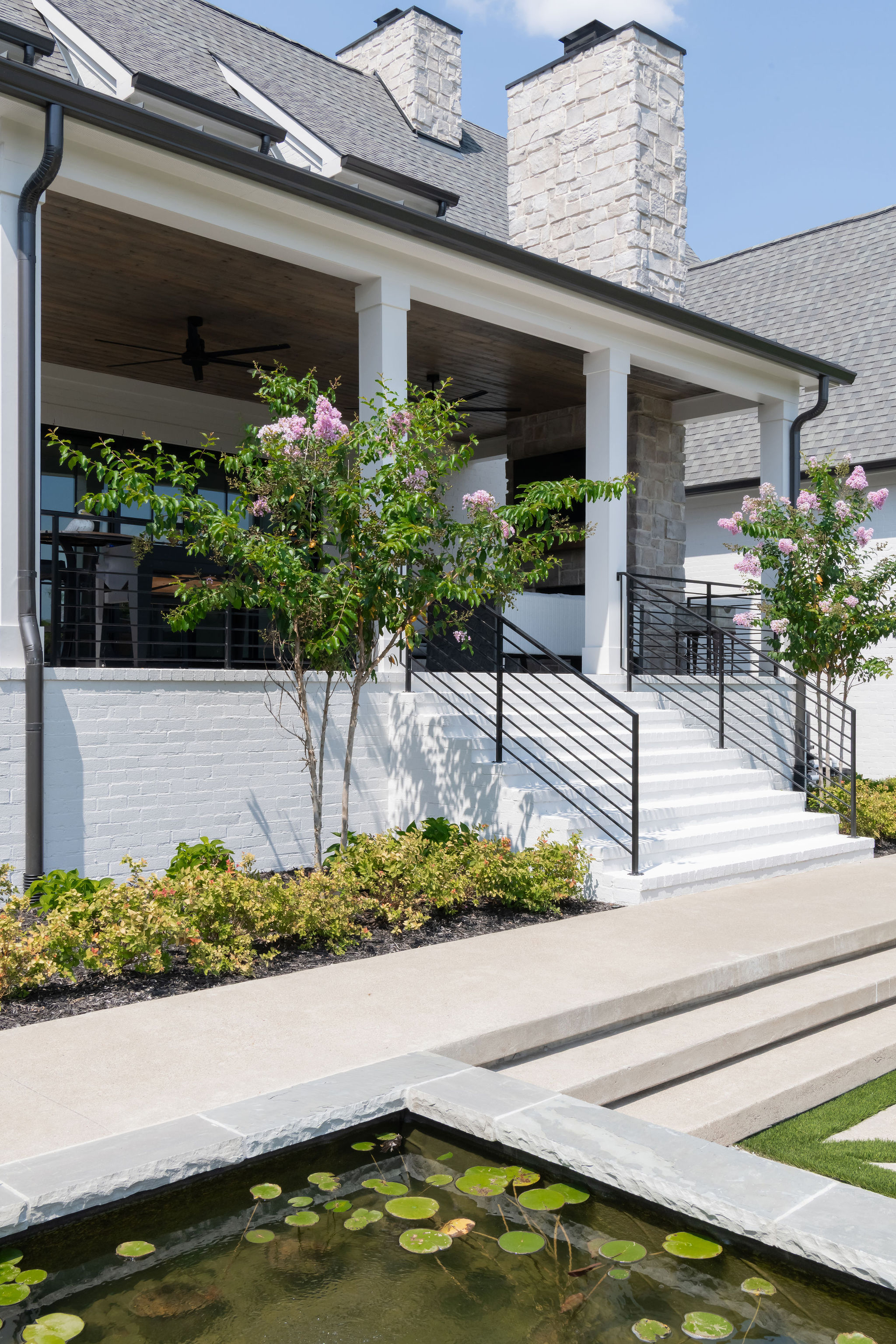 Well landscape porch with trees and shrubbery with pond-like water feature in foreground.
