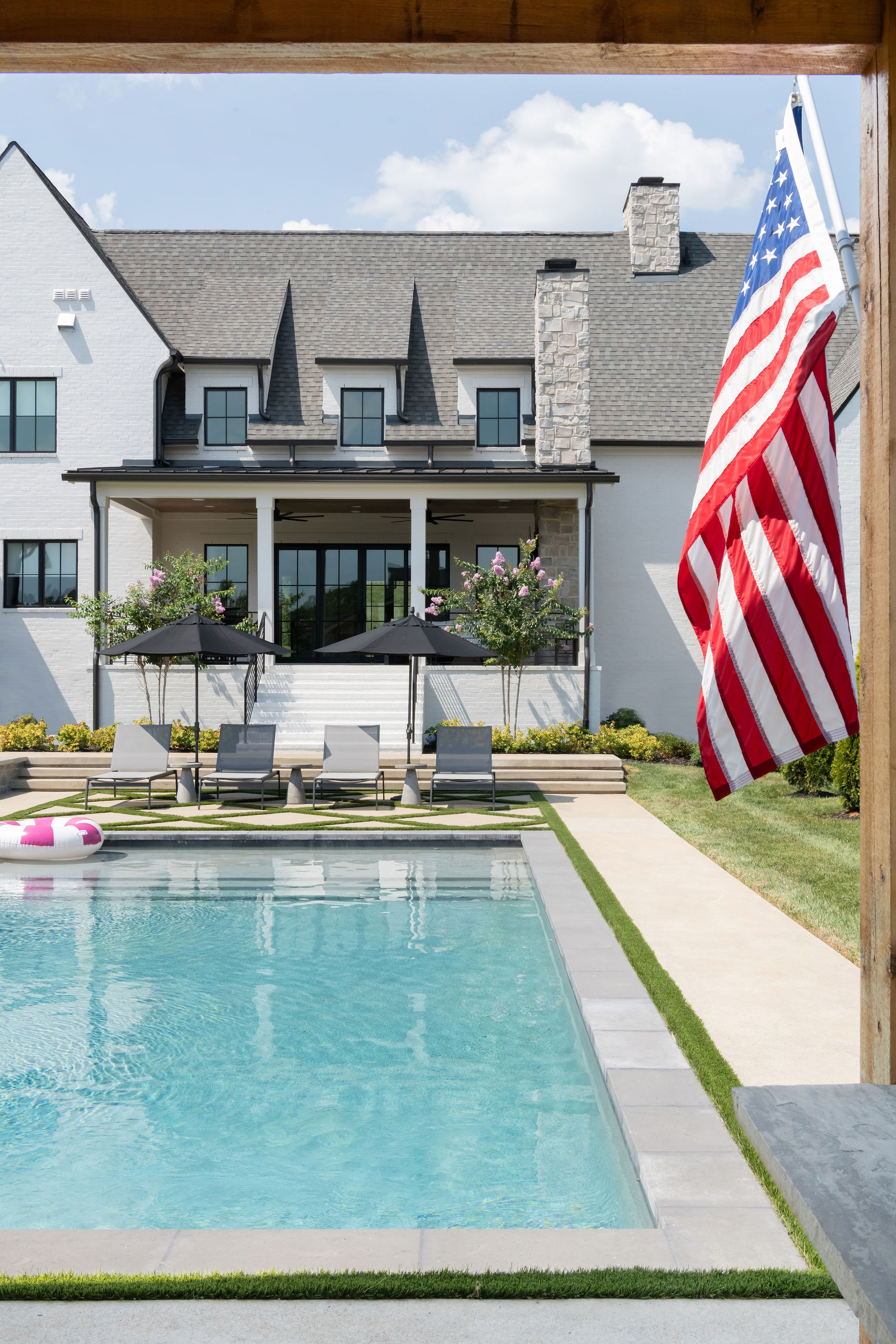Custom pool with American flag hanging in the left corner and large white home in the background.