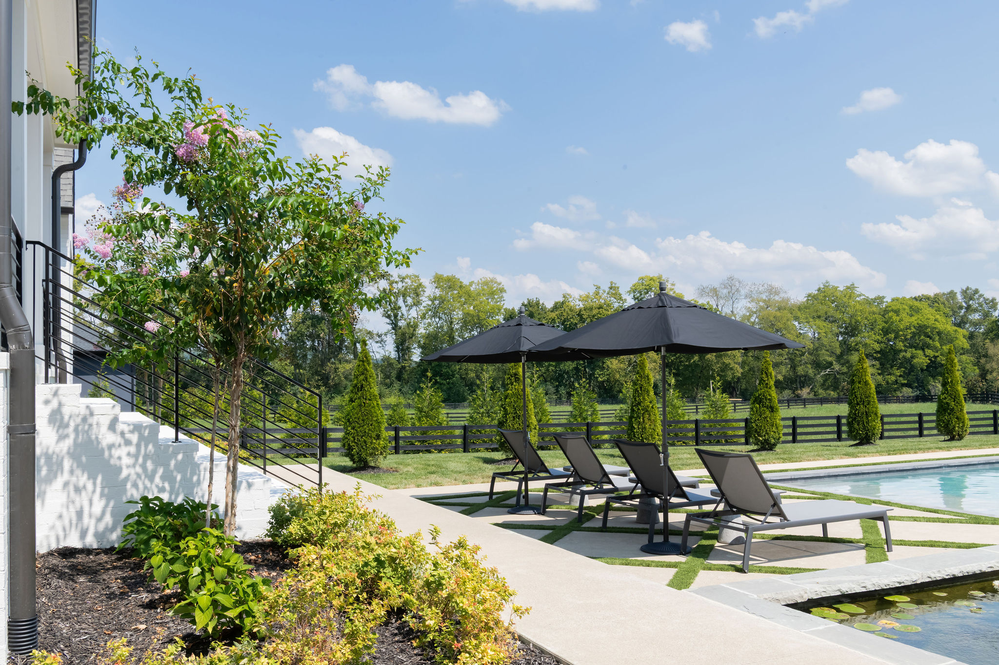 side view of patio furniture, walkway and landscape bushes overlooking a pool.