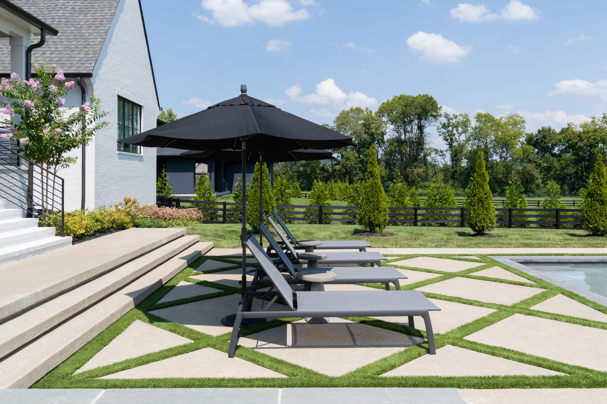Three patio chairs on large stone pavers with an umbrella shady the chairs.