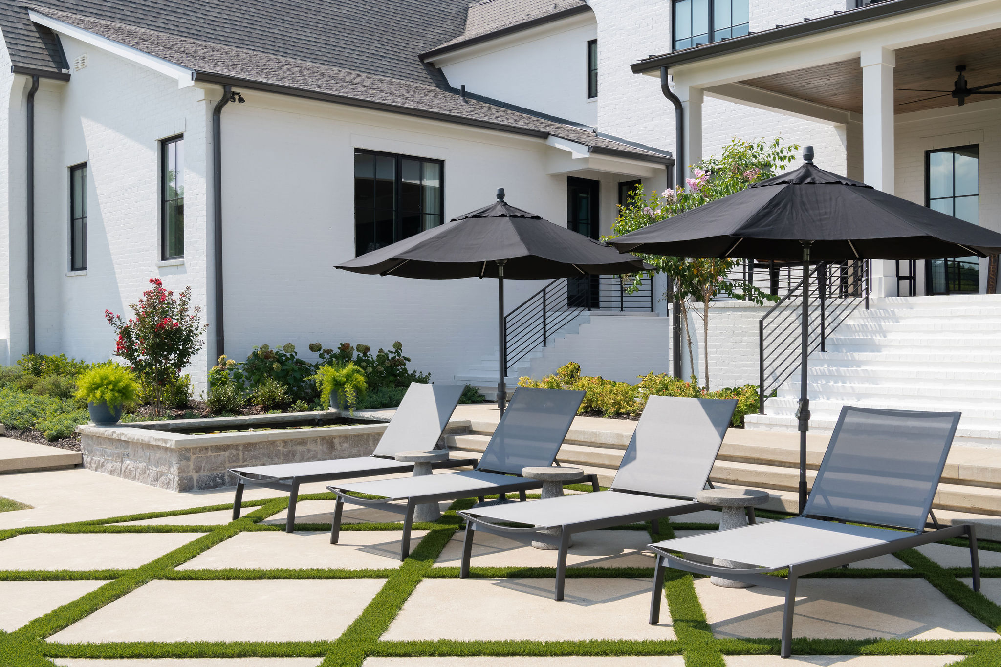 Front fiew of three patio chairs on large stone pavers with umbrellas shading the chairs.